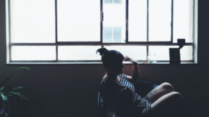 Woman sitting along in room in front of a large window - Childhood Trauma Survivors: Living to Tell the Tale